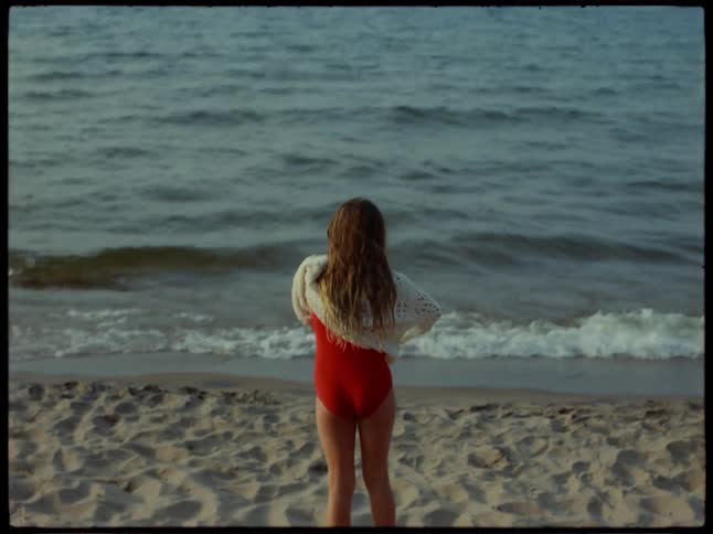 A girl removes her sweater and walks into the ocean