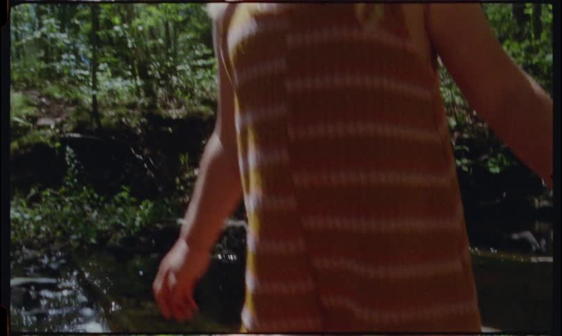 A blonde girl smiles as she steps out of a water stream unto a collection of rocks