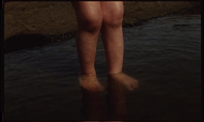 A blonde girl playfully steps into a shallow pool of water