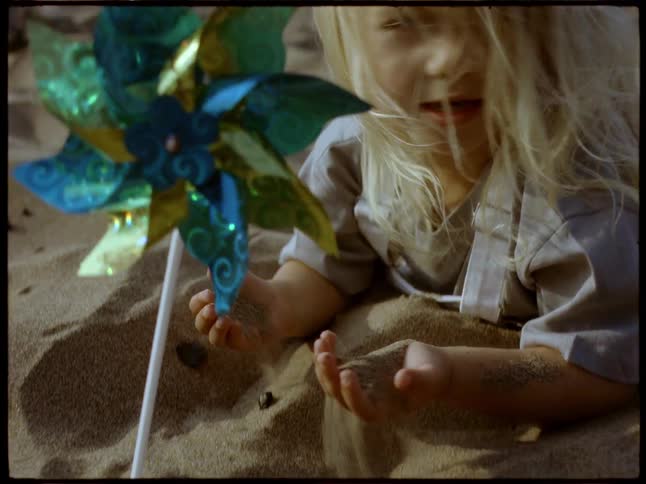 A young girl puts a blue pinwheel in the sand while playing on the beach