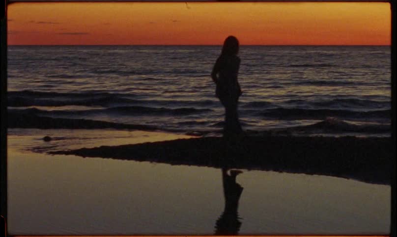 Silhouette of a woman walking on the sand of the beach against a reddish sky