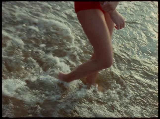 A girl child walks into the beach water barefooted at sunset