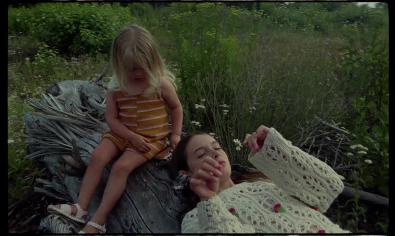 Two sisters are laying in the grass while playing with flowers near a forest