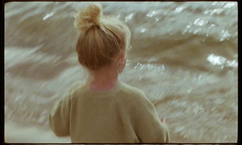 A blonde girl drops a scoop of sand and walks back to the seashore to rinse her hands