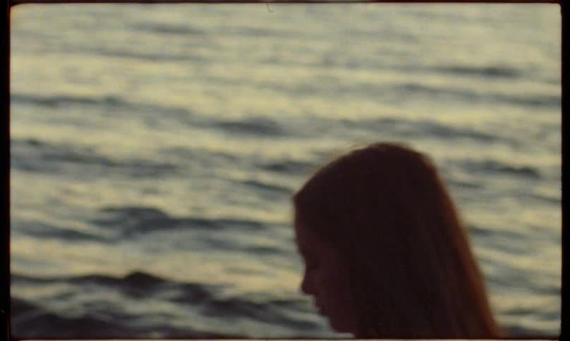 A young woman walks along the beach in profile at sunset silhouetted against the ocean