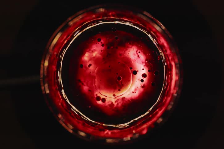 Top view of a glass with translucent red liquid containing small dark bubbles