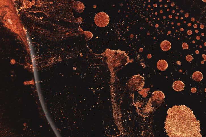 Rotating portions of an orange and black liquid rotate slowly releasing globs of orange