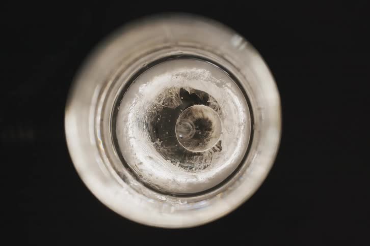A circular piece of ice seen from a topdown extreme closeup view inside a glass creates an abstract cosmiclike effect