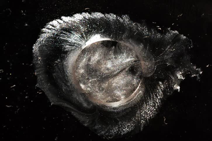 A highspeed macro shot captures the dramatic burst of a circular object creating a symmetrical splash against a dark background