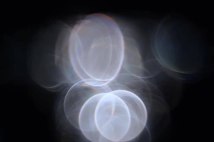 Some white circular shaped light flares on a black background and they are moving