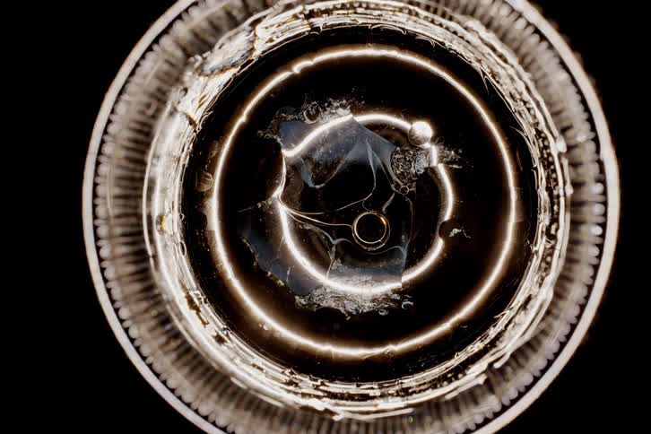 A macro shot of an abstract circular shape with light reflections resembling a lens or glass object viewed directly from above