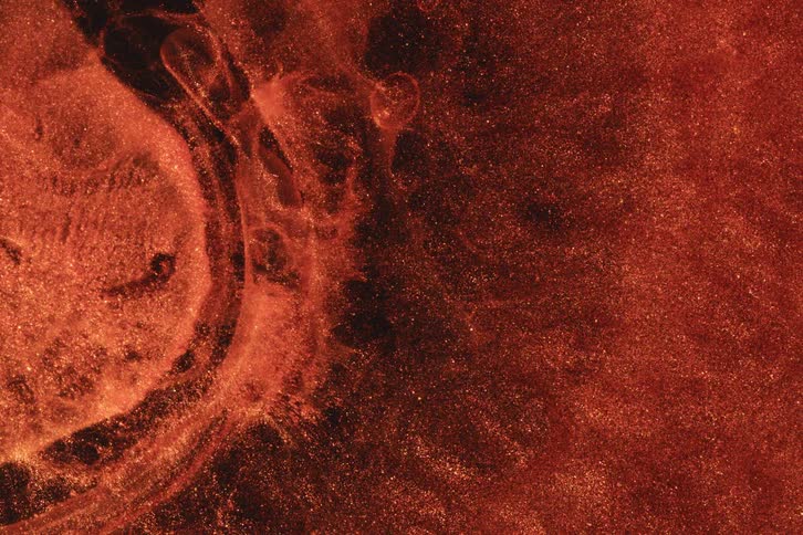 A textured extreme closeup shows swirling coppertoned forms evoking liquid or powder in magnified detail