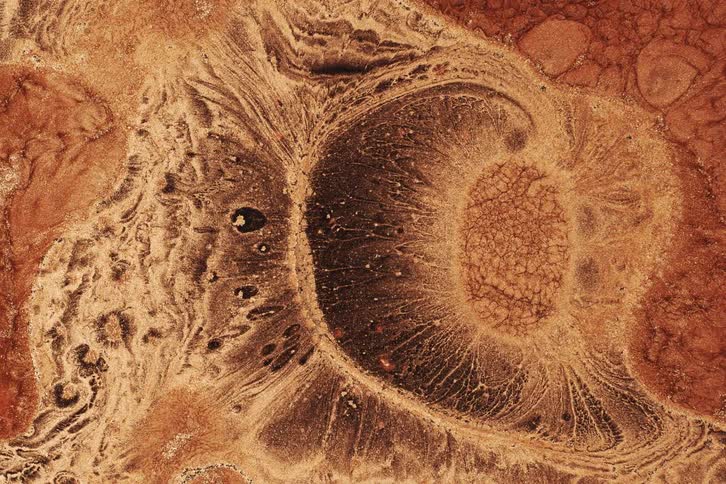 A swirling abstract texture in earthy tones resembles a cosmic explosion or fluid reaction captured in extreme closeup