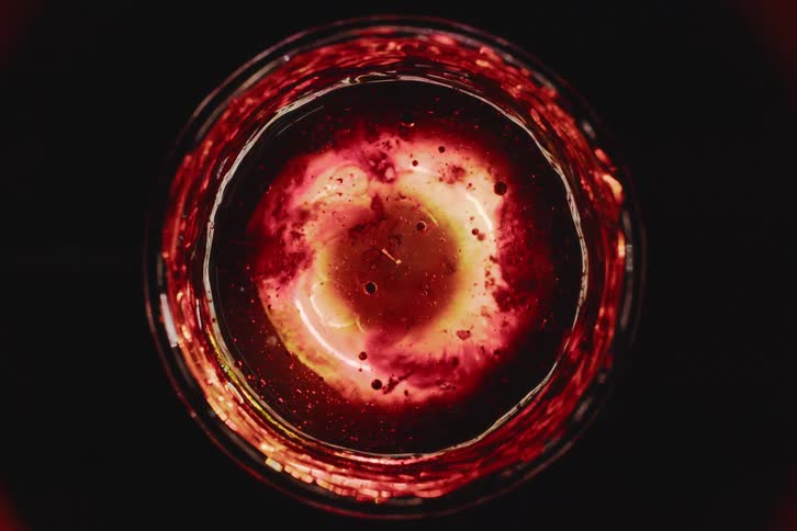 Extreme closeup of a glowing redhued liquid swirling in a glass forming a circular vortex pattern