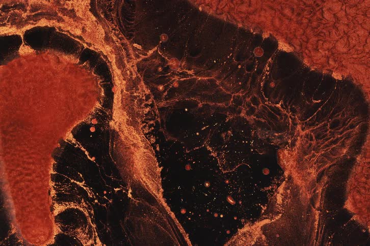 Brown metallic paint slowly drips into a black area below it creating abstract shapes