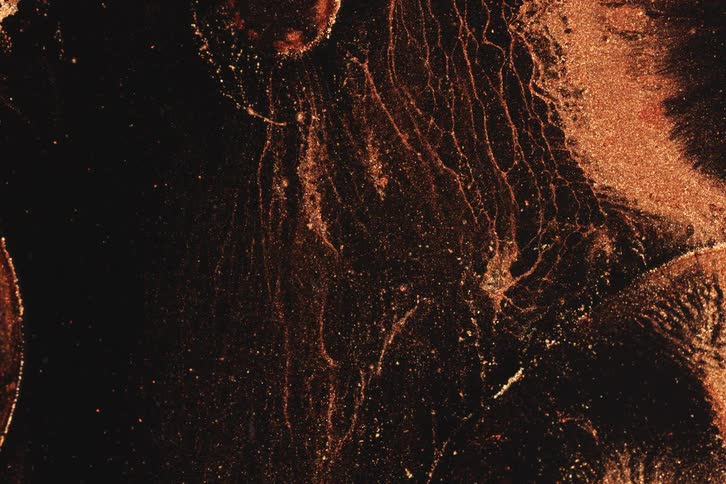 Copper like liquid lines and particles flow over a dark surface in an abstract veinlike pattern