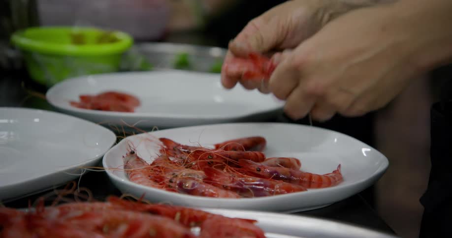 Picking up raw shrimp from a plater and placing them on a white plate