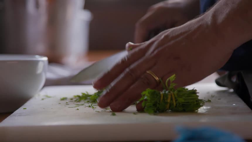 Chopping parsley on a white cutting board with sharp chef knife