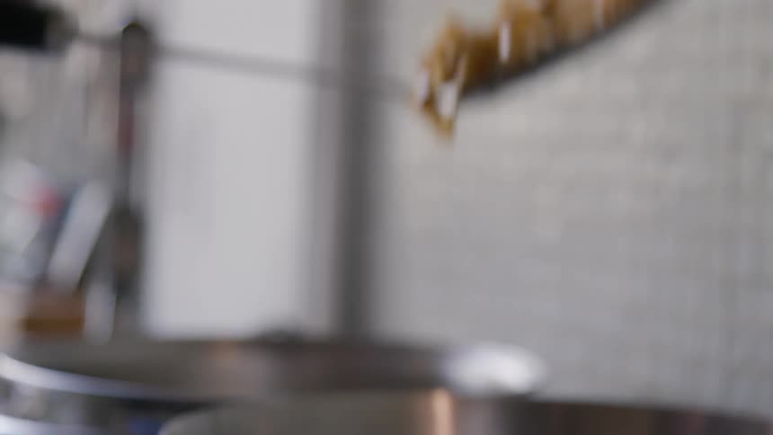 A closeup shot shows a spoonful of cooked food likely pasta or eggs being held above a cooking pan in a kitchen setting