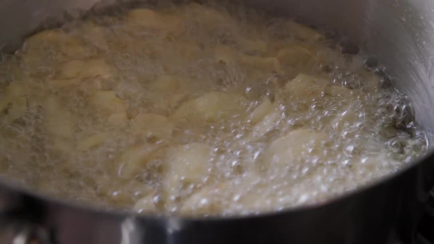 A skimmer stirs food in a pan with boiling water