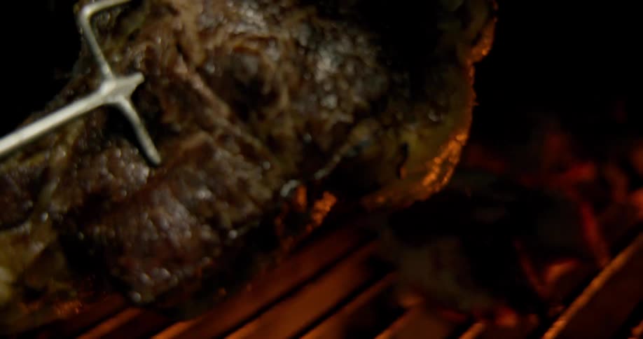 A closeup view of meat being grilled over open flames in a dark setting