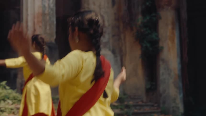 Young girls in traditional attire dance outdoors in front of an old stone structure