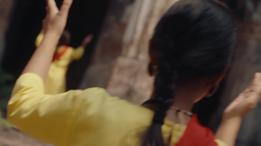 Women clap and dance in front of an ancient building during the day