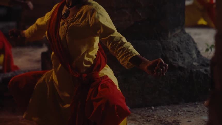 A person dressed in traditional attire performs a spiritual or cultural dance in a dimly lit outdoor setting