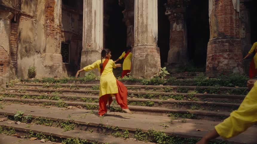 A group of women dance in front of an ancient structure during the day