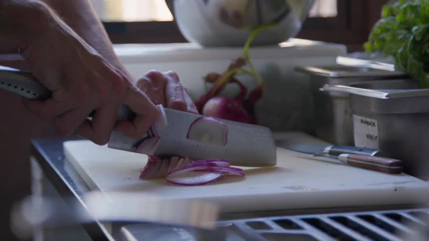 Slicing red onions with a sharp chef knife on white cutting board