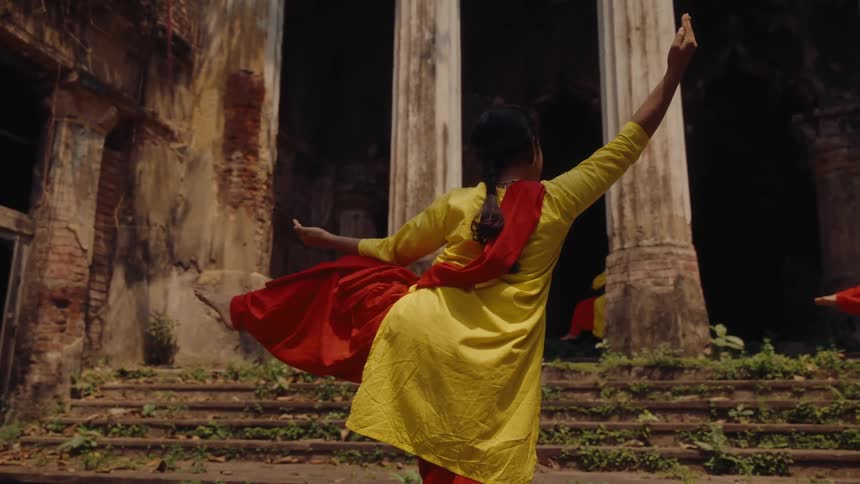 A group of women dance in front of an ancient structure during the day