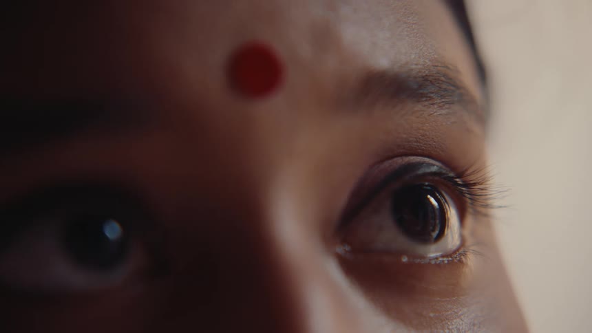 An extreme closeup of a womans eyes with a red bindi on her forehead captures an intense and contemplative expression