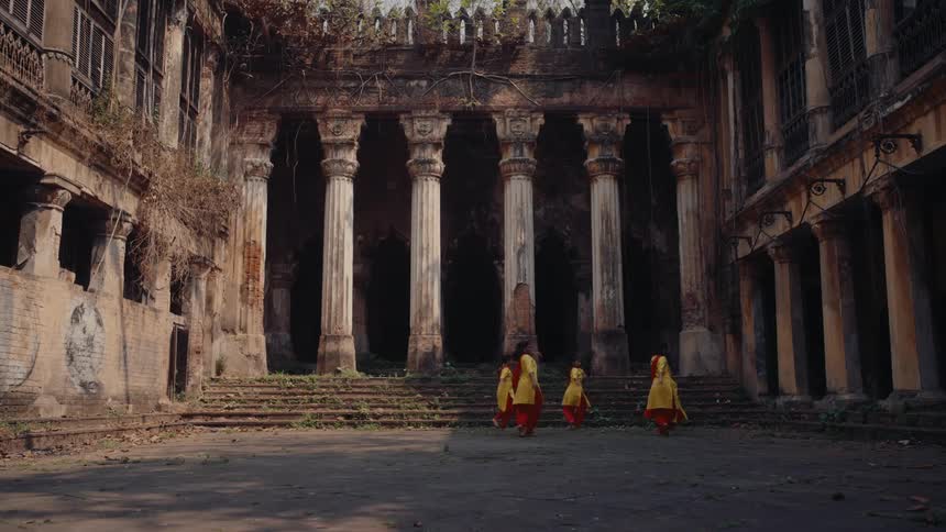 A group of women step from side to side as the dance in a courtyard