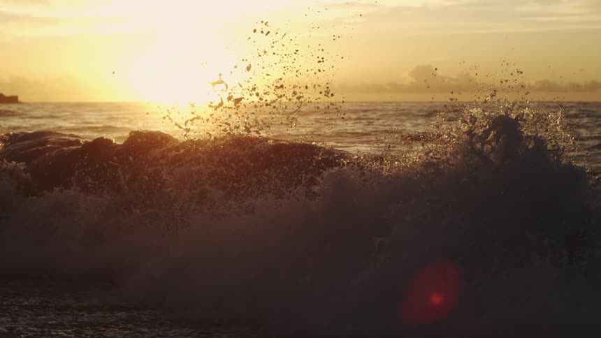 Water splashes in the air as waves roll into shore and the sun shines on the horizon