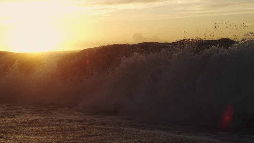 Waves splash as they roll in to shore as the sun shines on the horizon