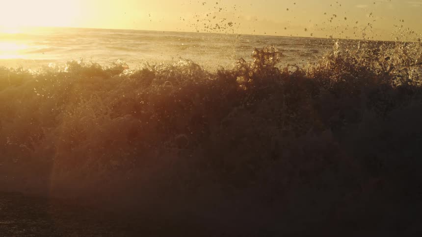 Waves splash and foam as they roll into shore as the sun shines on the horizon