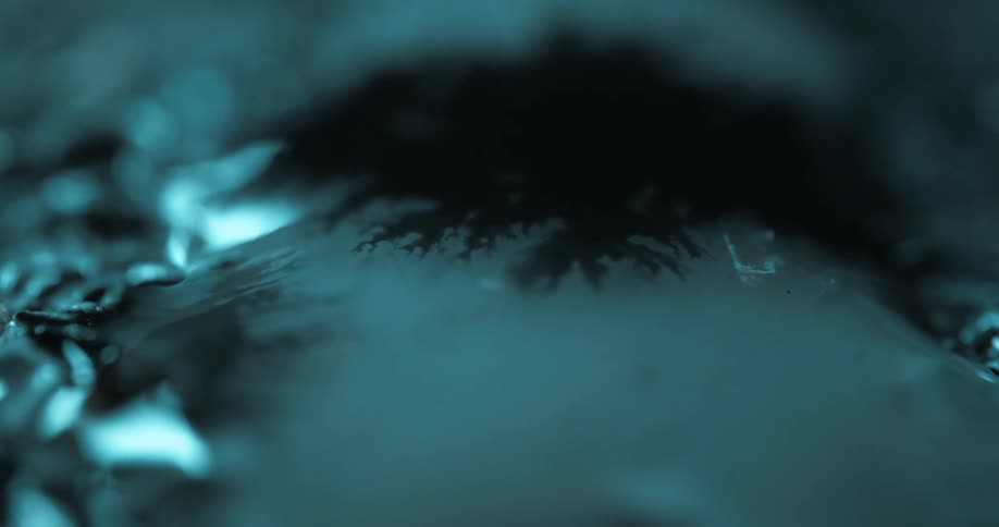 Closeup of a dark viscous liquid gradually spreading across a cooltoned surface maintaining its thick slowmoving consistency