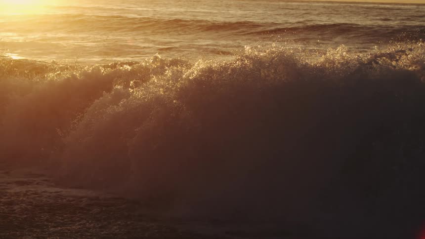 Waves splash as they roll in to shore and the sun shines brightly on the horizon