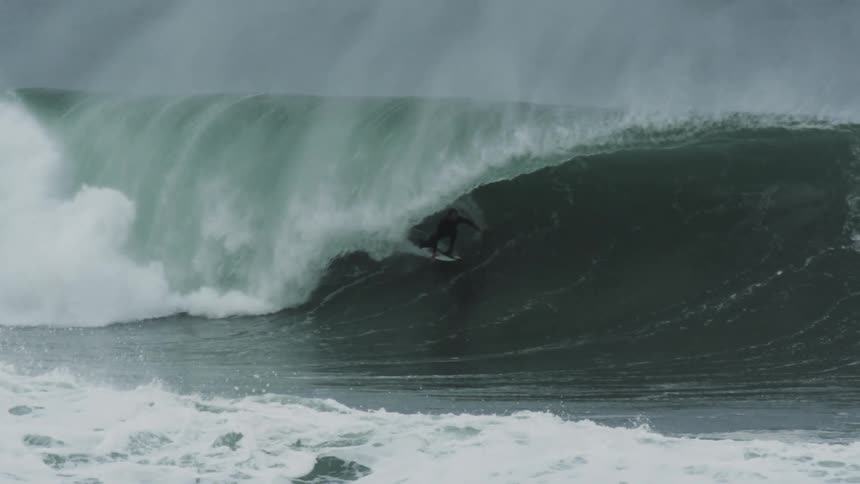 A surfer skillfully rides inside the barrel of a large powerful ocean wave as it begins to close over them