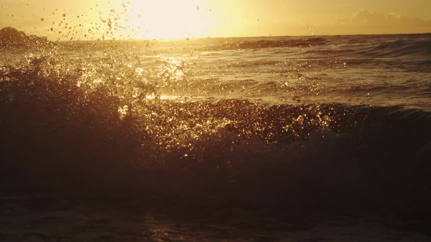 Waves splash as they roll in to shore and the sun shines on the horizon
