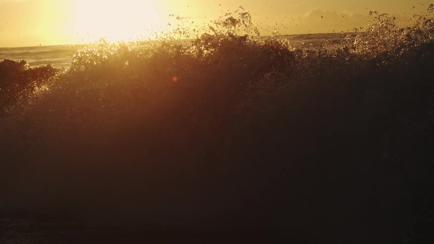 Water splashes as waves roll into shore as the sun shines brightly through clouds on the horizon
