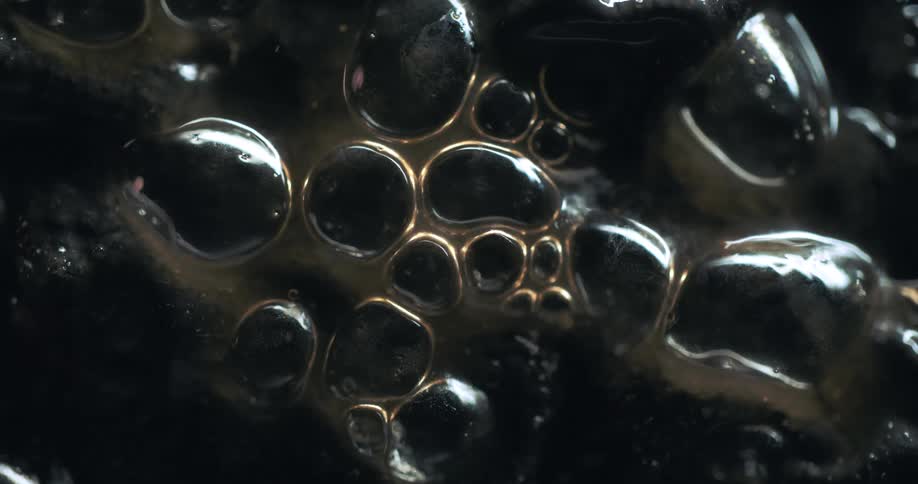 Thick dark liquid bubbles slowly rise and morph in a closeup shot creating an abstract and organic texture