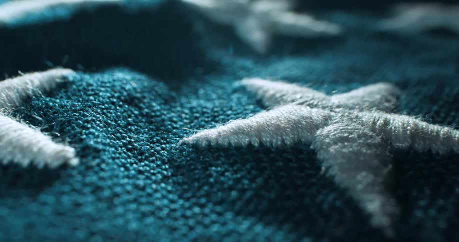 A slow motion pan over large white fabric stars on a bumpy blue canvas showing a closeup of a part of an americanflag