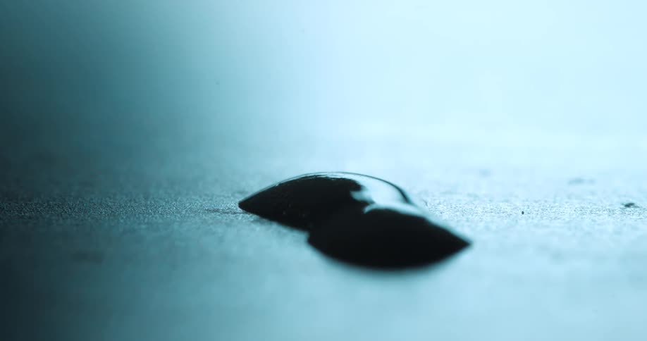 Two dark drops rest on a blue surface in closeup