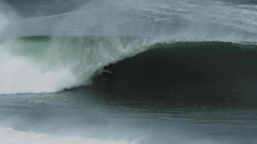 Surfer rides a huge wave and stays on his surfboard as it curls overhead