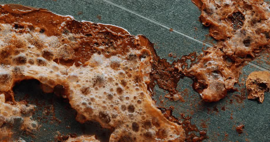 A closeup shot of a foamy decaying rustcolored organic or chemical substance spreading over a textured surface