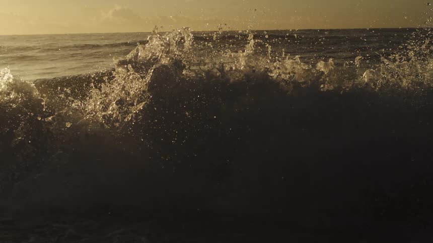 Waves splash into the air and water sparkles in the sunlight as they roll in to shore