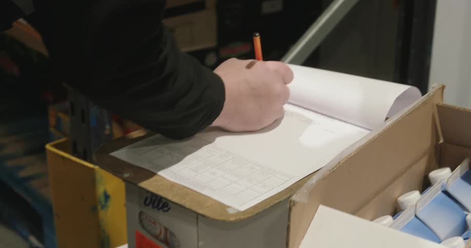 A man is writing on his clipboard while taking inventory in the warehouse