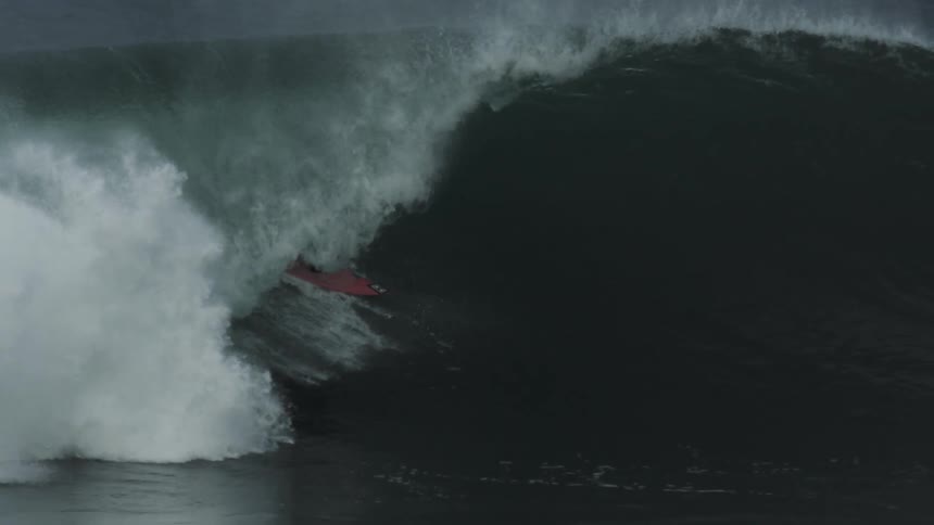 Surfer rides a huge wave and stays on his surfboard as it curls overhead