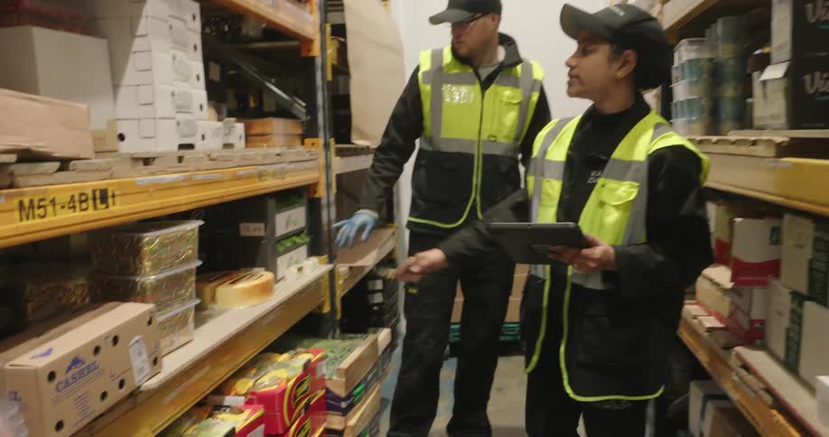 Two workers counting goods on the shelves inside a warehouse at night